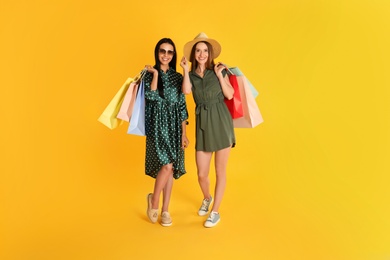 Photo of Beautiful young women with paper shopping bags on yellow background