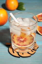 Photo of Delicious refreshing drink with sicilian orange, fresh fruits and green leaves on light blue wooden table
