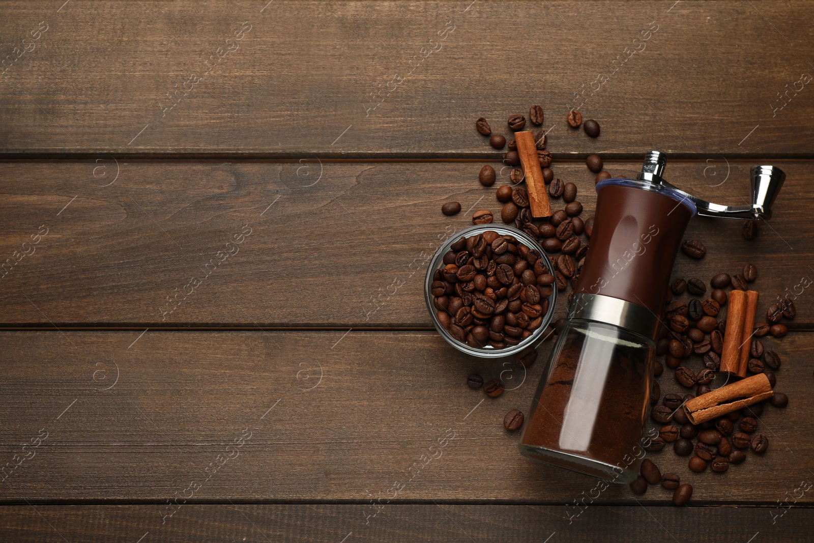 Photo of Manual coffee grinder with powder, beans and cinnamon on wooden table, flat lay. Space for text