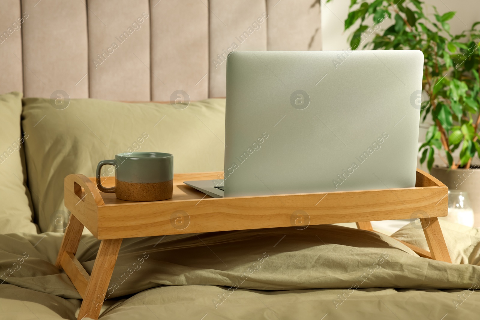 Photo of Wooden tray with modern laptop and cup of aromatic drink on bed indoors