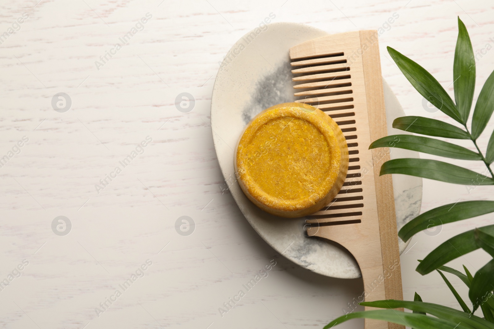 Photo of Solid shampoo bar, hair comb and green branch on white wooden table, top view. Space for text