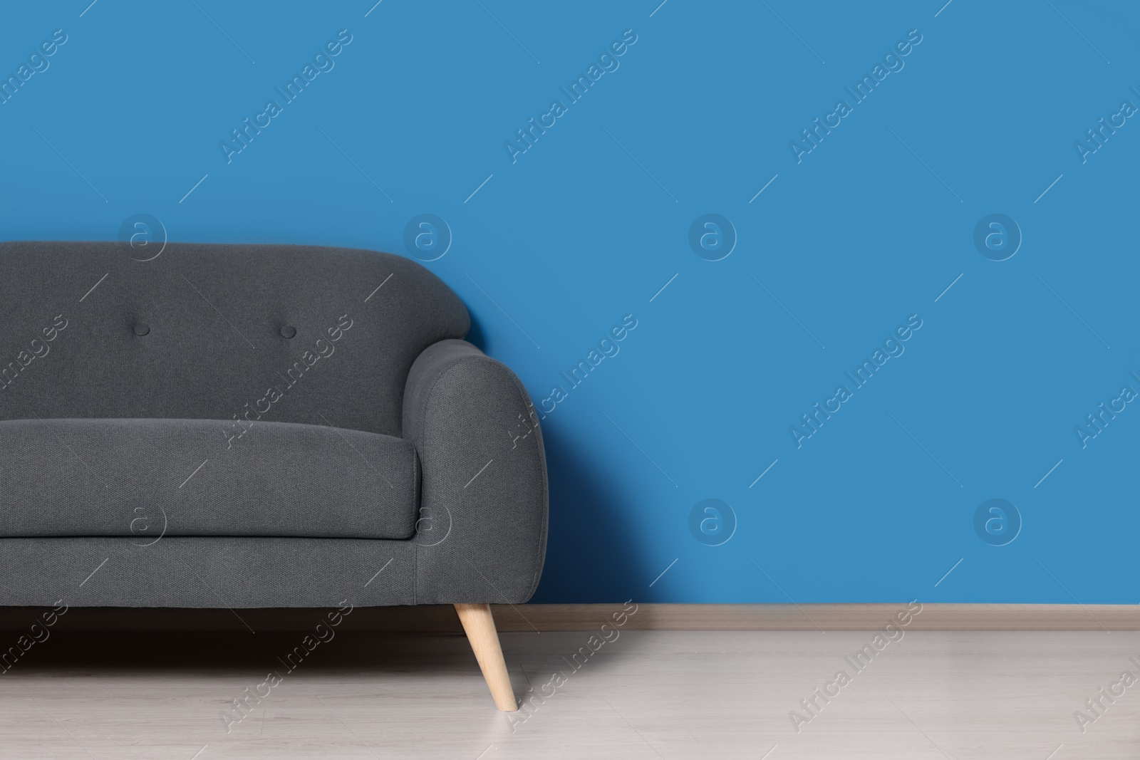 Photo of Stylish grey sofa near blue wall in room. Interior design