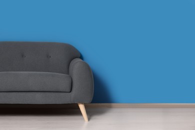 Photo of Stylish grey sofa near blue wall in room. Interior design