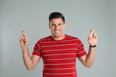 Photo of Man with crossed fingers on grey background. Superstition concept