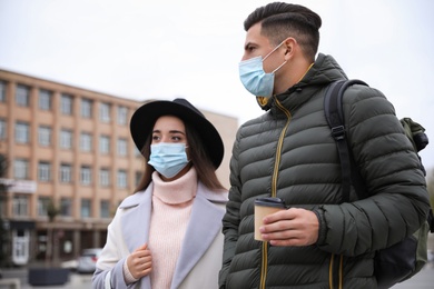 Photo of Couple in medical face masks walking outdoors. Personal protection during COVID-19 pandemic