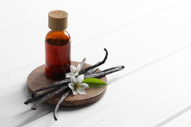 Photo of Vanilla pods, flowers, leaf and bottle with essential oil on white wooden table, closeup. Space for text