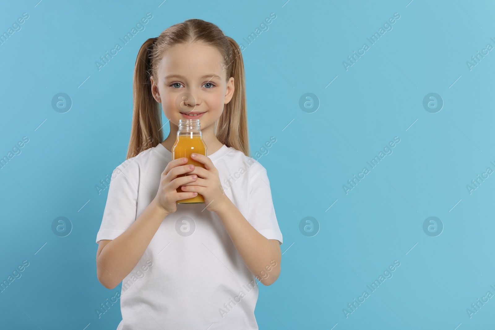 Photo of Cute little girl with bottle of fresh juice on light blue background, space for text