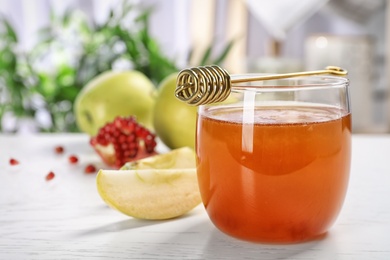 Photo of Glass of honey, apples, pomegranate and dipper on light table. Rosh Hashanah holiday