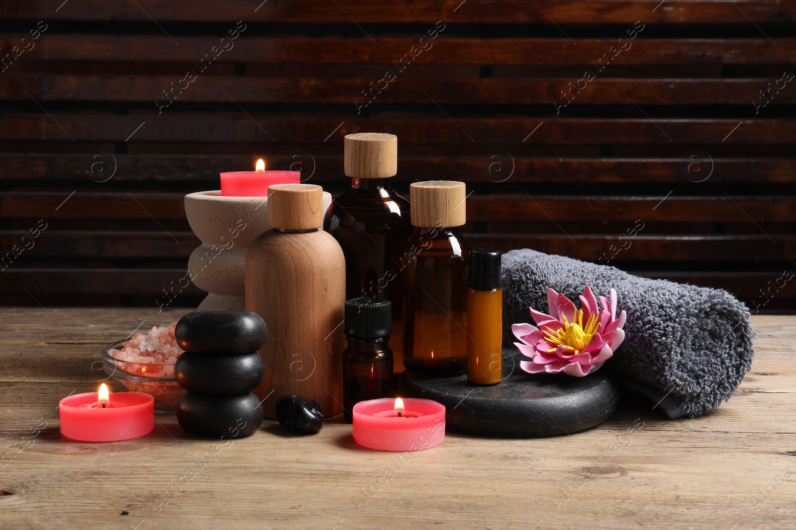 Photo of Different aromatherapy products, spa stones, towel and flower on wooden table