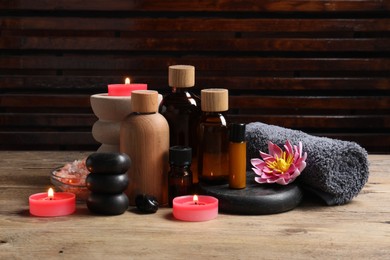 Different aromatherapy products, spa stones, towel and flower on wooden table