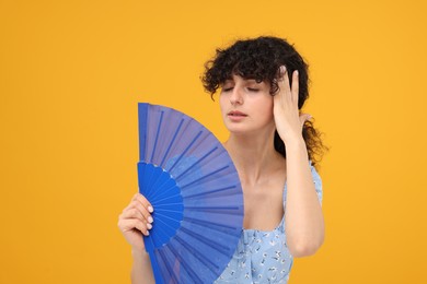Photo of Woman with hand fan suffering from heat on orange background