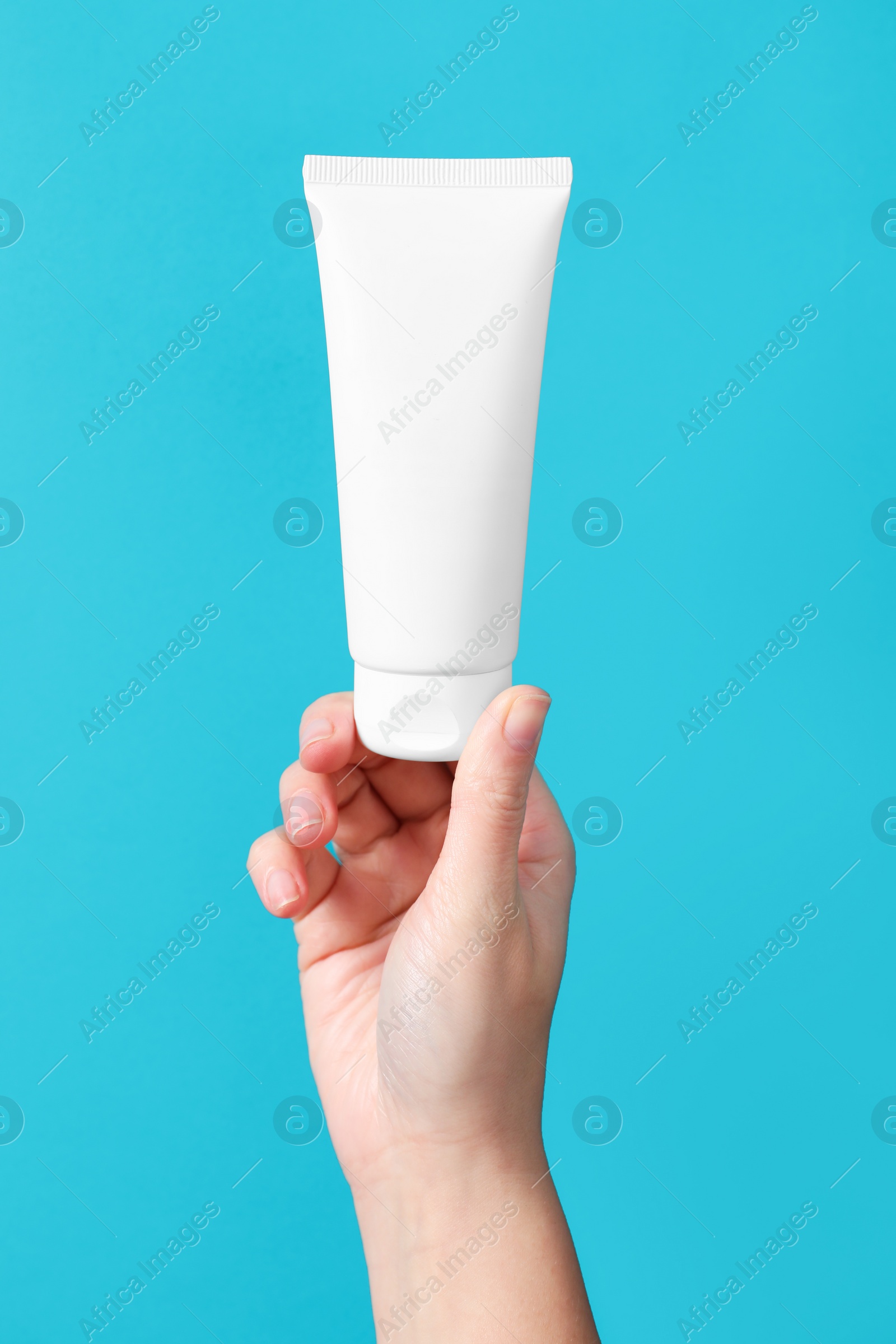 Photo of Woman with tube of hand cream on light blue background, closeup