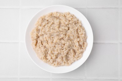 Delicious barley porridge in bowl on white tiled table, top view