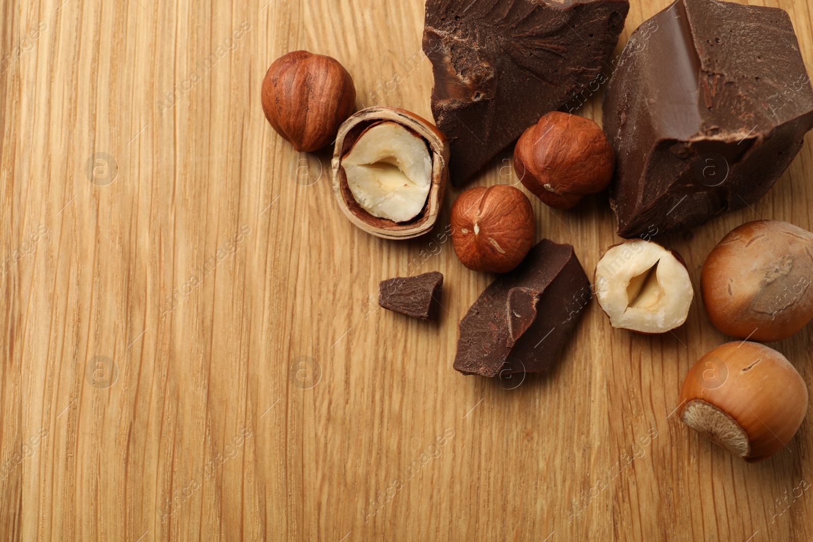 Photo of Delicious chocolate chunks and hazelnuts on wooden table, flat lay. Space for text