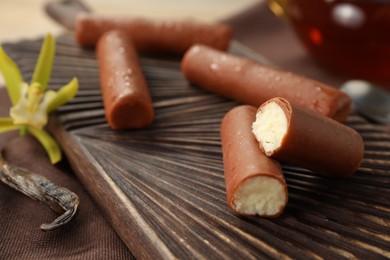 Photo of Glazed curd cheese bars, vanilla pods and flower on table, closeup