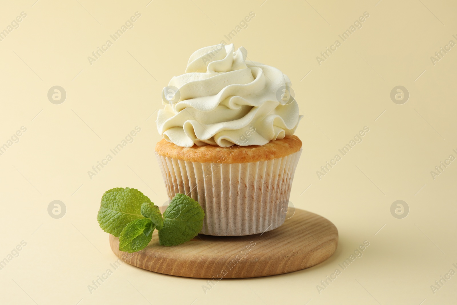 Photo of Tasty vanilla cupcake with cream and mint on pale yellow background