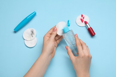 Photo of Woman using makeup remover, closeup. Cotton pads, lipstick and mascara on light blue background, top view