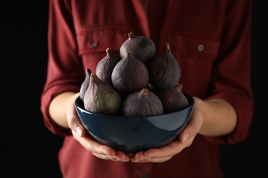 Photo of Woman holding bowl with tasty raw figs on black background, closeup