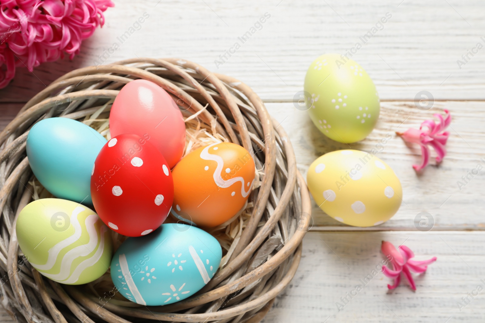 Photo of Flat lay composition of wicker nest with colorful painted Easter eggs and flower on table