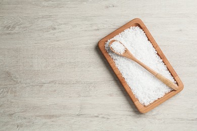 Photo of Plate and spoon with natural sea salt on light wooden table, top view. Space for text