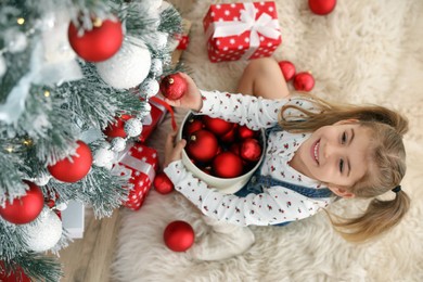 Cute little girl decorating Christmas tree at home, above view