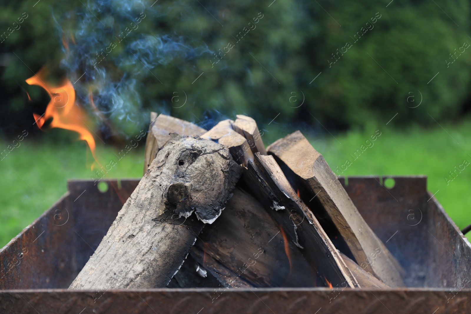 Photo of Metal brazier with burning firewood outdoors, closeup