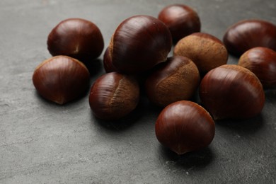 Photo of Roasted edible sweet chestnuts on grey textured table, closeup