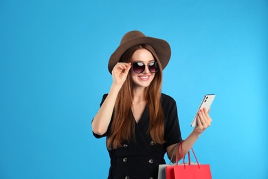 Photo of Beautiful young woman with paper shopping bags and smartphone on light blue background