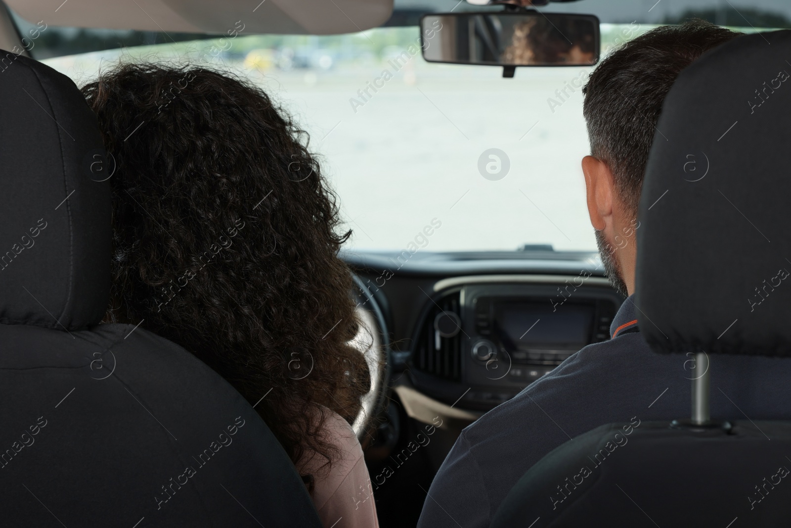 Photo of Driving school. Student during lesson with driving instructor in car, back view