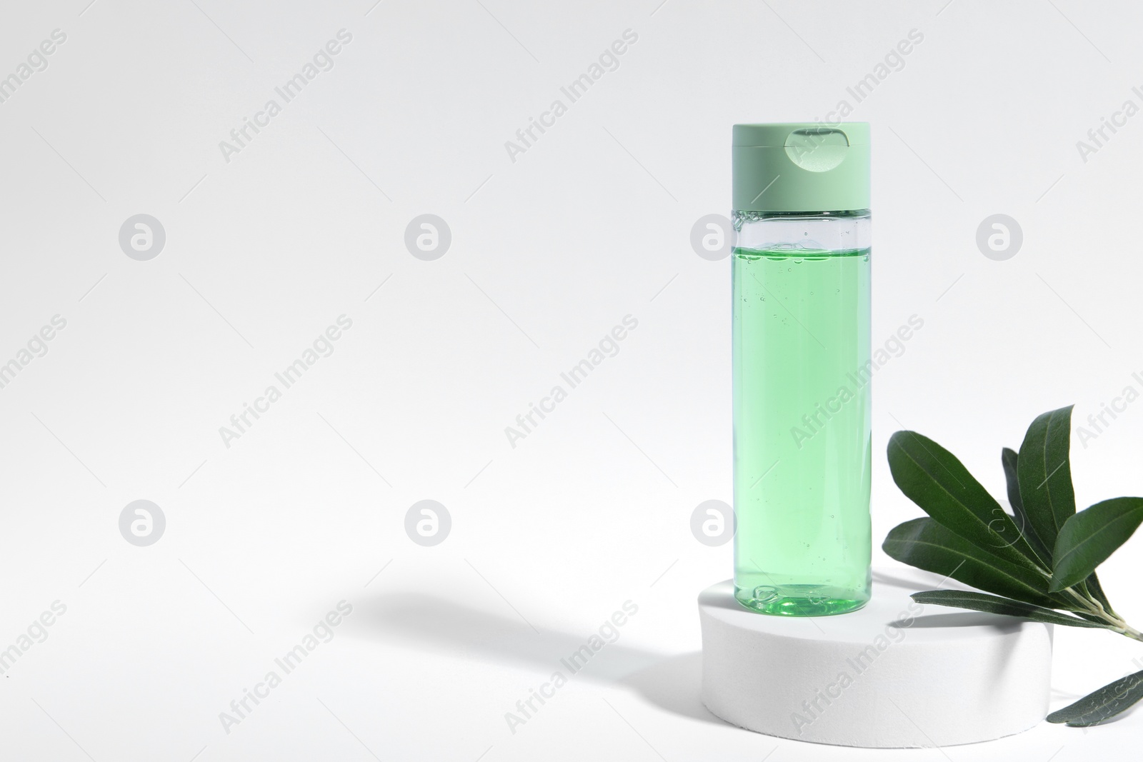 Photo of Bottle with cosmetic product and green leaves on white background, space for text