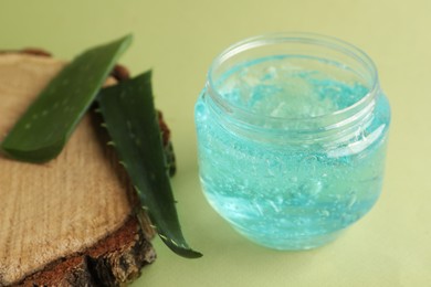 Photo of Jar of blue cosmetic gel and aloe on green background