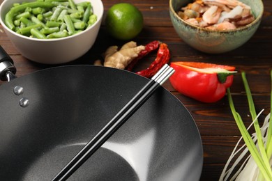 Photo of Black wok, chopsticks and products on wooden table, closeup