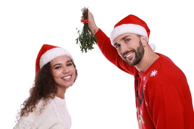 Photo of Portrait of lovely couple in Santa hats under mistletoe bunch on white background