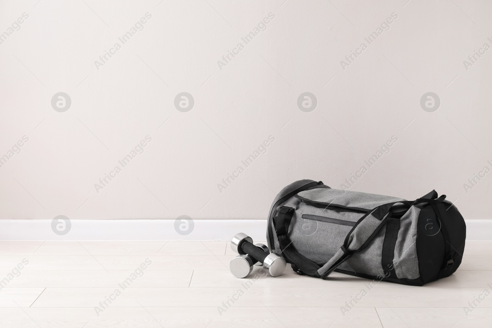 Photo of Grey sports bag and dumbbells on floor near light wall, space for text