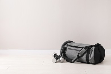 Photo of Grey sports bag and dumbbells on floor near light wall, space for text