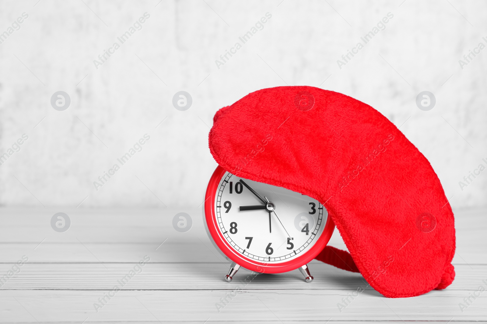 Photo of Soft sleep mask and alarm clock on white wooden table. Space for text