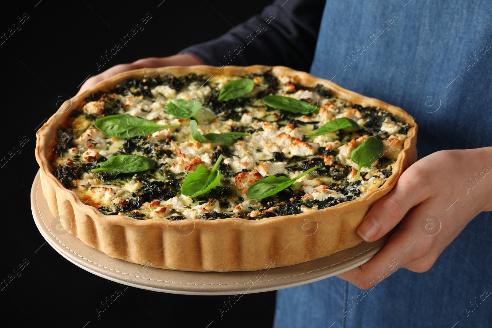 Photo of Woman holding delicious homemade spinach quiche on dark background, closeup