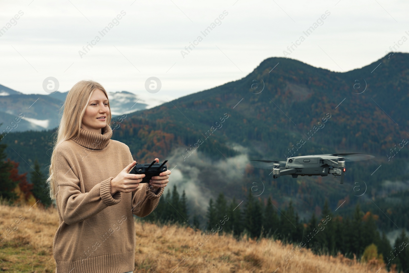 Photo of Young woman operating modern drone with remote control in mountains