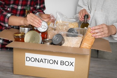 Photo of Women taking food out from donation box at wooden table, closeup