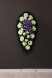 Photo of Funeral wreath of plastic flowers near hanging on dark grey wall indoors