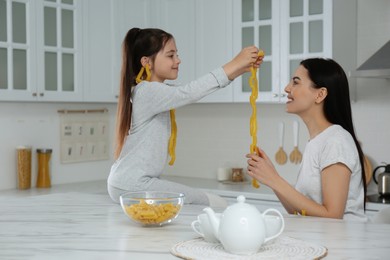 Photo of Young mother and her daughter with necklaces made of pasta having fun in kitchen