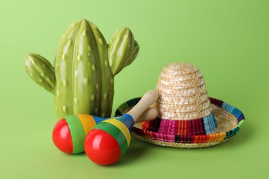 Colorful maracas, toy cactus and sombrero hat on light green background. Musical instrument