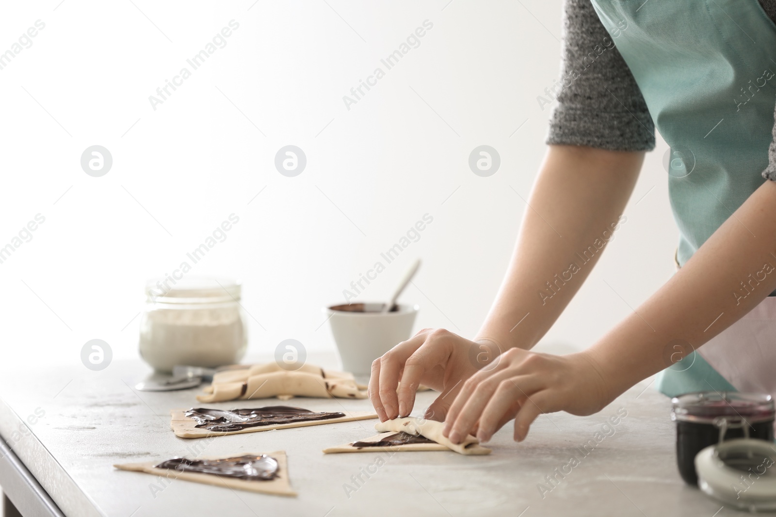 Photo of Woman preparing tasty croissants with chocolate paste at table in kitchen