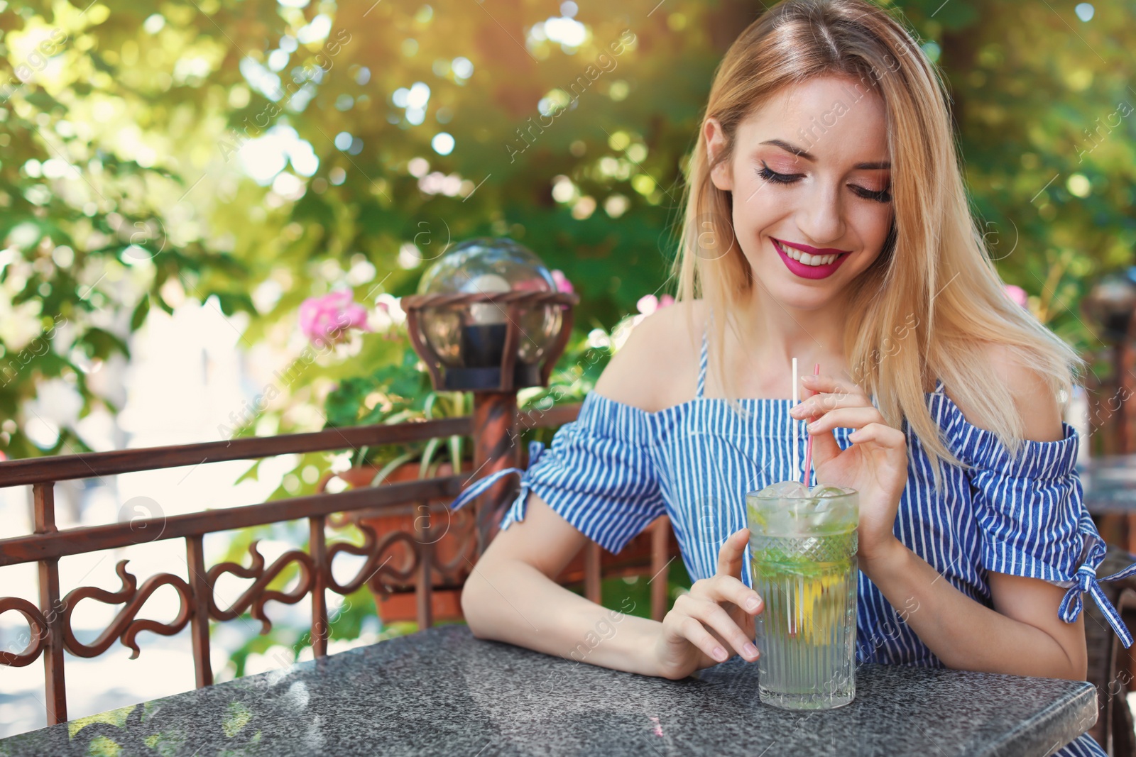 Photo of Young woman with glass of tasty lemonade at table in cafe, outdoors. Natural detox drink