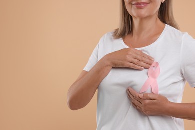 Breast cancer awareness. Woman with pink ribbon doing self-examination on light brown background, closeup. Space for text