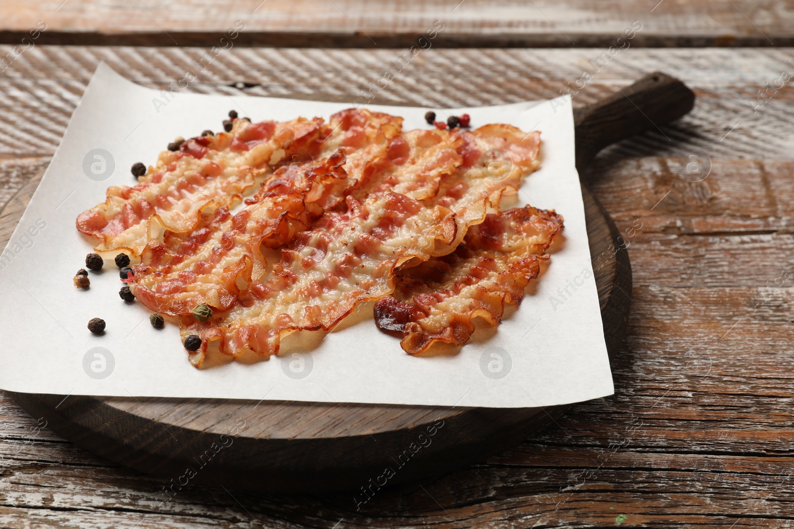 Photo of Delicious fried bacon slices on wooden table