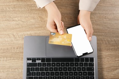 Photo of Online payment. Woman using credit card and smartphone with blank screen near laptop at wooden table, top view