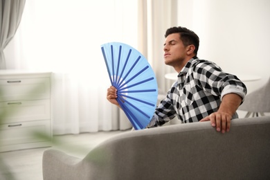 Photo of Man with hand fan sitting on sofa. Summer season