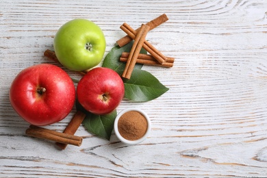 Fresh apples with cinnamon sticks and powder on wooden table, top view