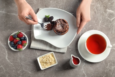 Woman eating delicious fresh fondant with hot chocolate at table, top view. Lava cake recipe